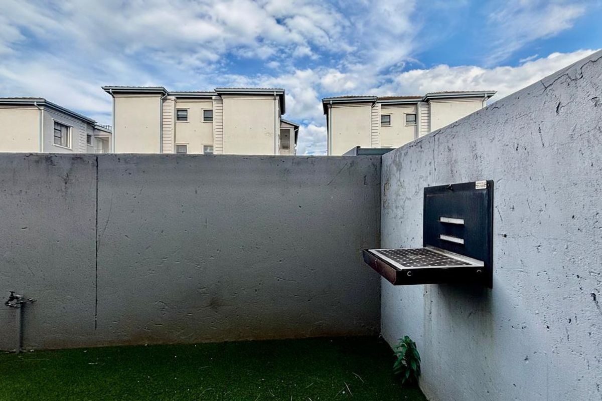 A private rear courtyard area featuring a wall-mounted braai, artificial lawn, and an external water tap, enclosed by a boundary wall.