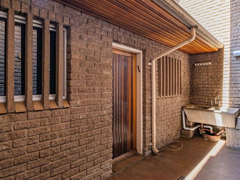 Outdoor laundry area featuring a utility sink, brick wall construction, and timber ceiling slats, providing a functional space for household tasks.