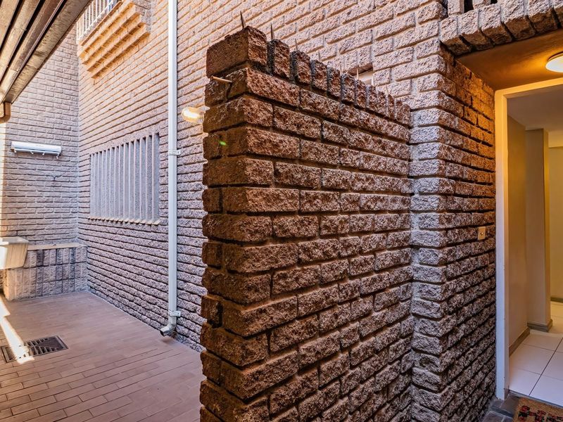 A functional outdoor utility area featuring a brick wall, tiled flooring, and a built-in utility sink, providing practical space for laundry or maintenance tasks.