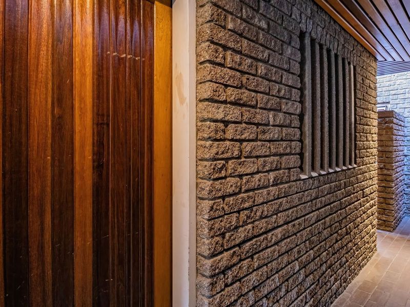 A welcoming townhouse entrance featuring a solid timber door, textured exposed brick wall, and a warm slatted timber ceiling with recessed lighting.