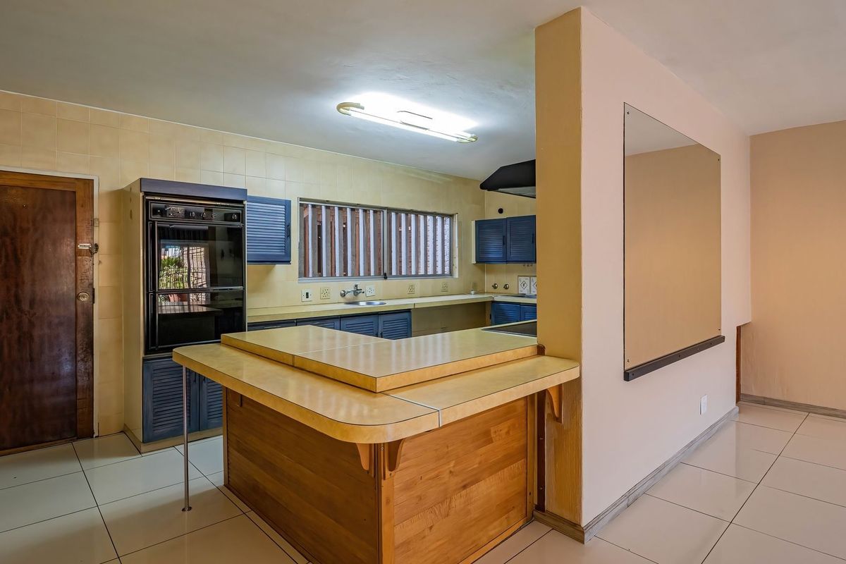 A spacious, empty kitchen featuring built-in cabinetry, a double oven, extractor fan, and tiled finishes, offering a functional layout ready for modernization.