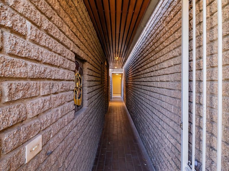 A narrow, well-maintained hallway featuring exposed brick walls, a timber slat ceiling, and tiled flooring, leading to an interior entrance.