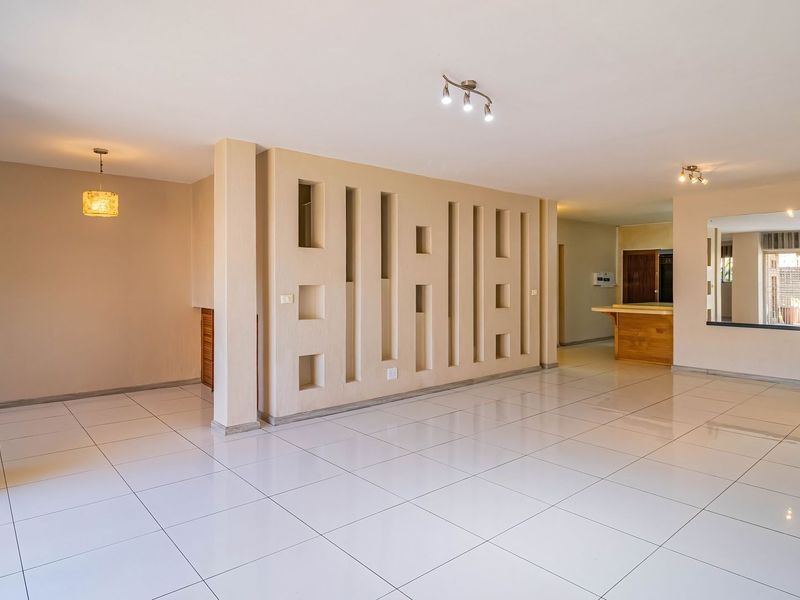 Spacious open-plan living area featuring polished tiled floors, a unique decorative partition wall, and a built-in breakfast bar, offering a versatile layout.