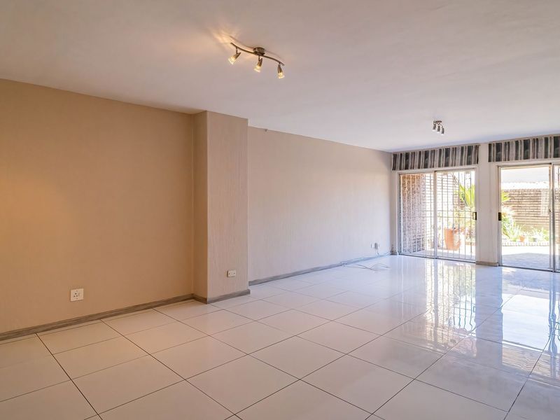 A spacious, empty living area featuring polished white floor tiles, neutral walls, and large sliding glass doors providing access to the outdoor patio area.