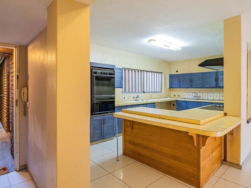 Open plan kitchen featuring blue cabinetry, built-in oven, hob, and a breakfast bar, adjacent to a tiled hallway leading to an outdoor walkway.