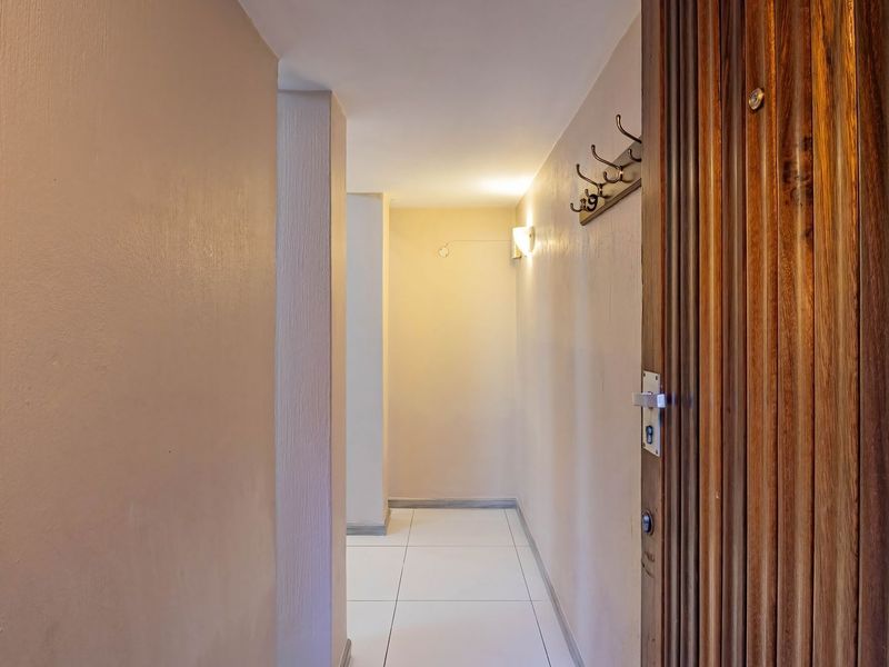A clean and bright entrance hallway featuring tiled flooring, warm wall-mounted lighting, and a solid wood front door.