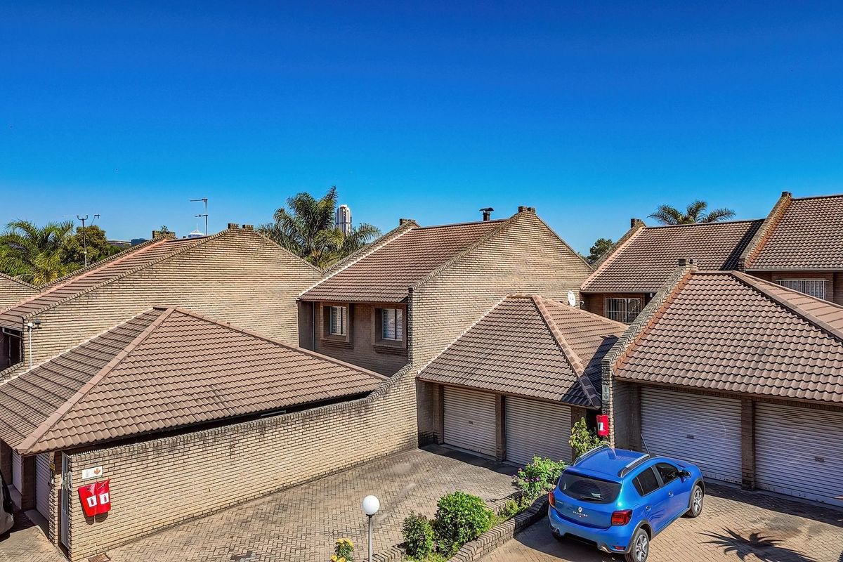 An elevated aerial view of a townhouse complex featuring brick facades, tiled roofs, and paved driveway access with multiple garage units.