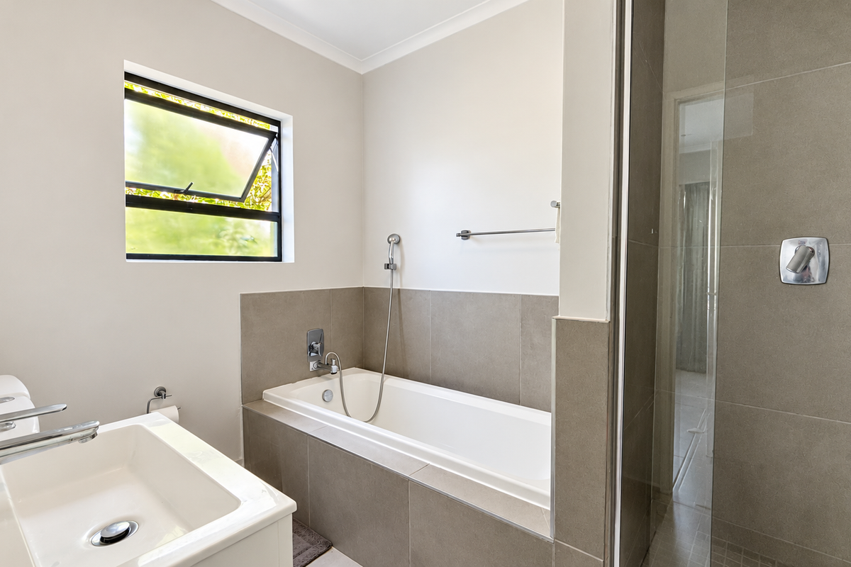 A clean, modern bathroom featuring a built-in bathtub, a separate glass-enclosed shower, and a contemporary basin with chrome fixtures.