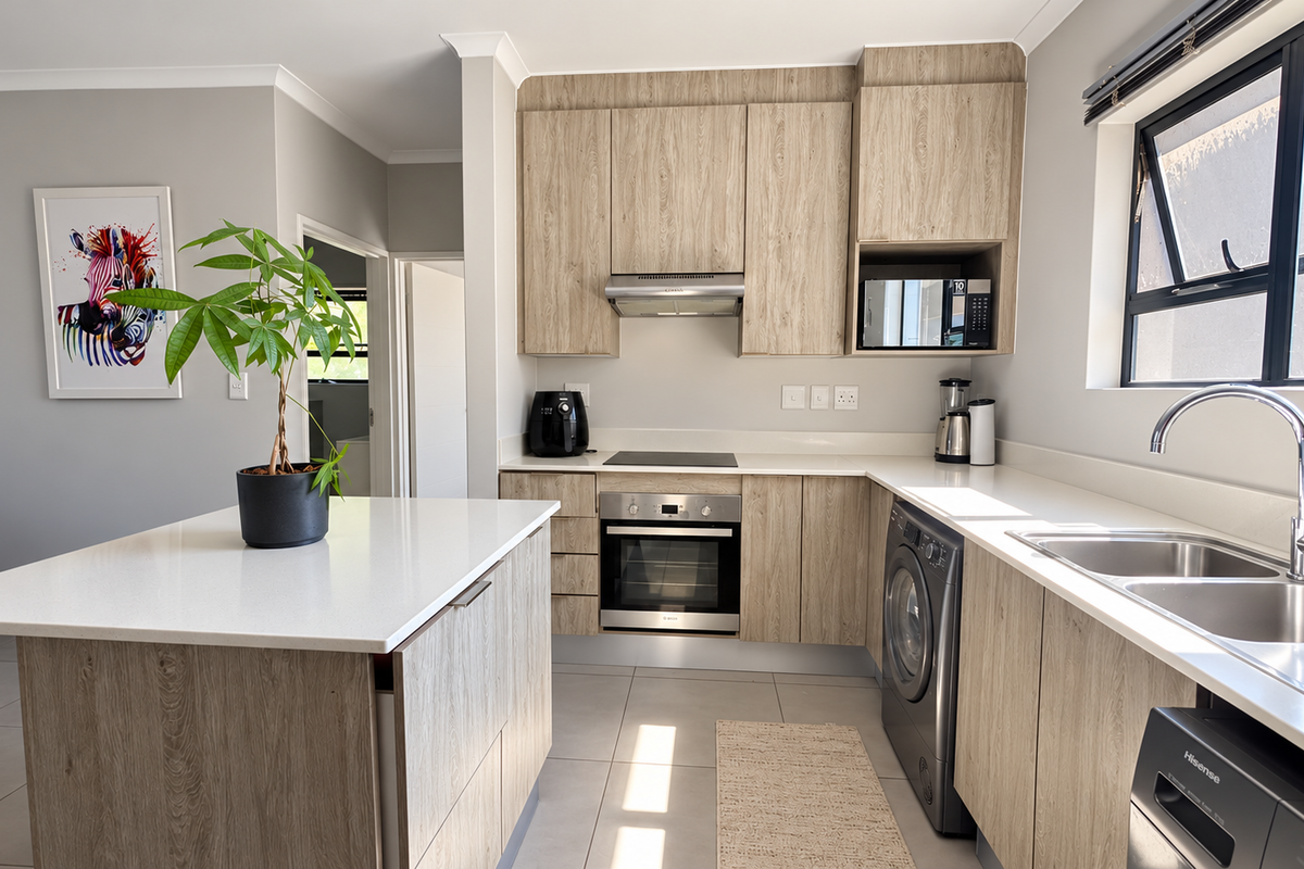 Modern kitchen featuring light wood-grain cabinetry, stone countertops, a central island, and integrated appliances including an oven, hob, and extractor fan.