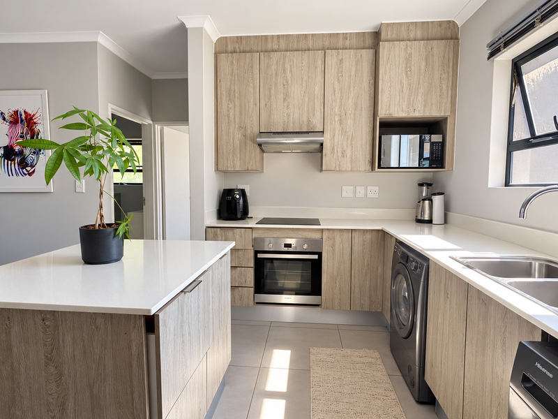 Modern kitchen featuring light wood-grain cabinetry, stone countertops, a central island, and integrated appliances including an oven, hob, and extractor fan.