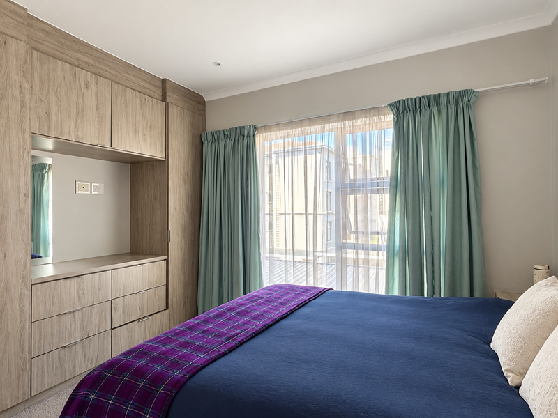 A well-maintained bedroom featuring extensive built-in wooden cabinetry with integrated vanity and storage, complemented by large windows allowing natural light.