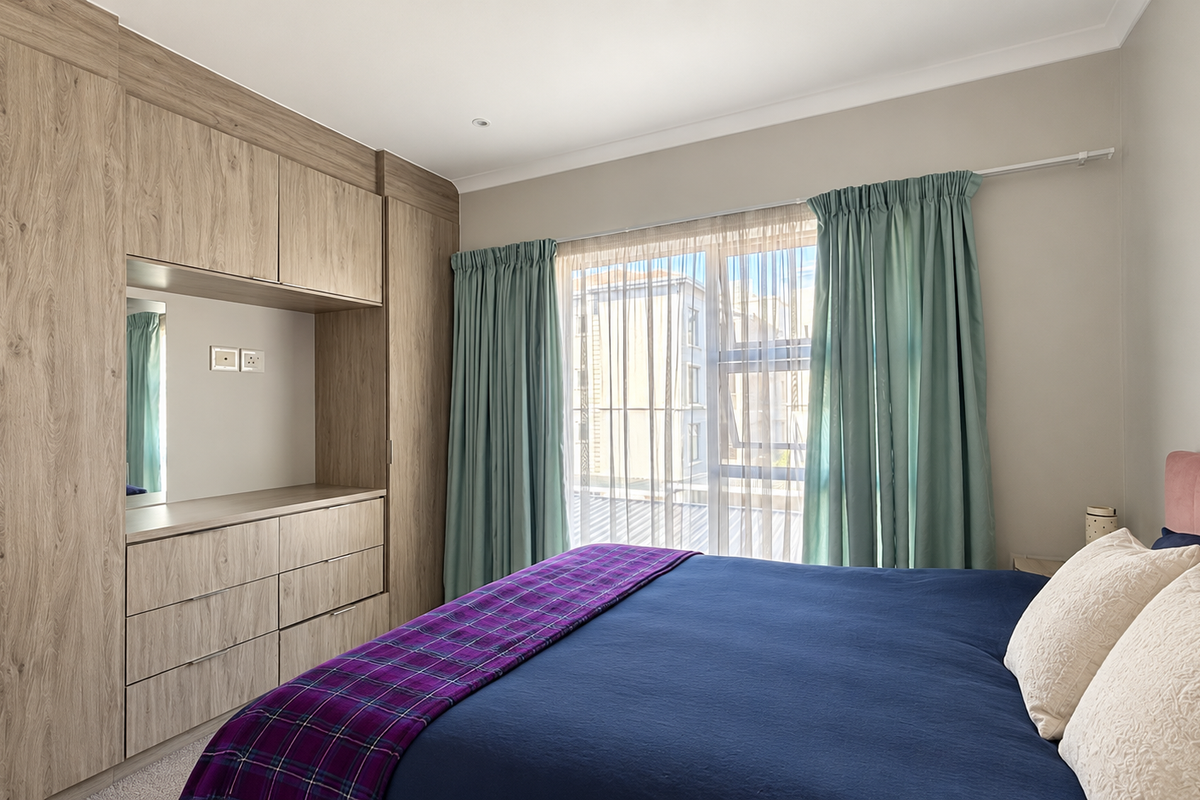 A well-maintained bedroom featuring extensive built-in wooden cabinetry with integrated vanity and storage, complemented by large windows allowing natural light.