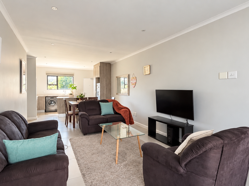 A bright open-plan living area featuring tiled floors, recessed lighting, and a modern kitchen with integrated cabinetry and appliances.