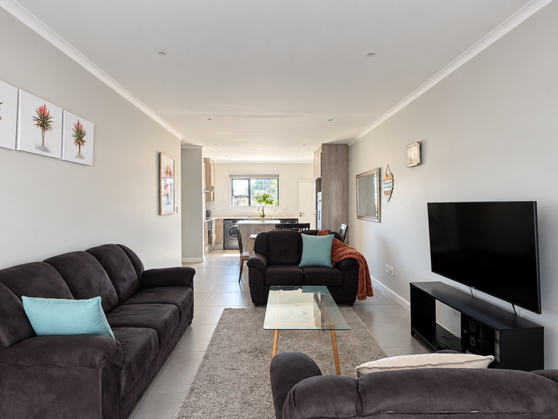A bright open-plan living and kitchen area featuring neutral tiled floors, recessed lighting, and a functional kitchen layout with modern cabinetry.
