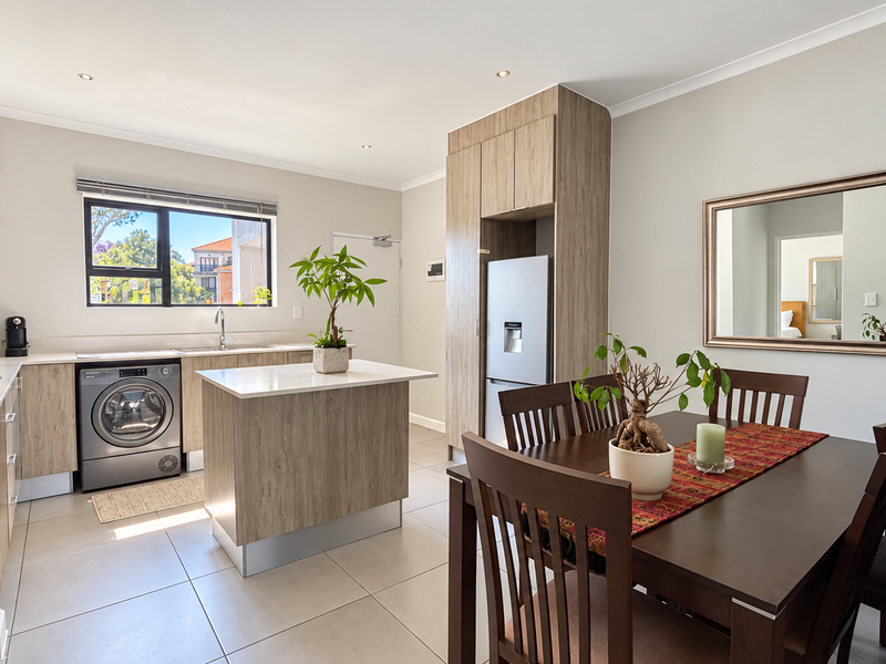 Modern open-plan kitchen and dining area featuring light wood cabinetry, stone countertops, tiled flooring, and integrated appliance housing.