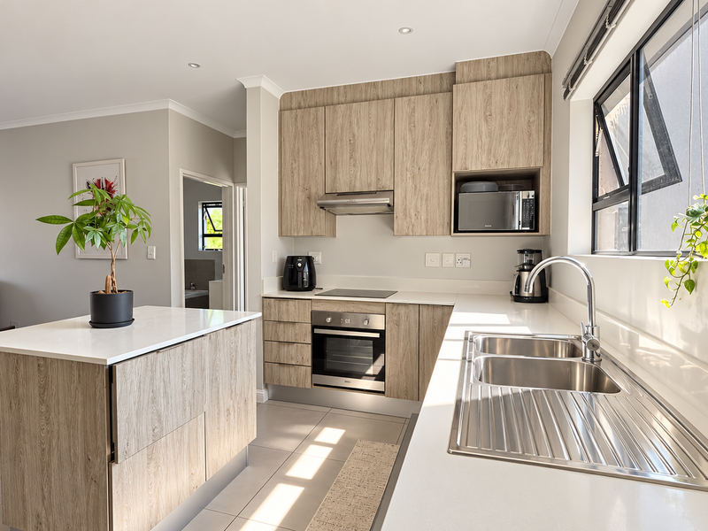 Modern open-plan kitchen featuring light wood-grain cabinetry, stone countertops, integrated appliances, and a functional kitchen island, seamlessly connecting to the dining area.