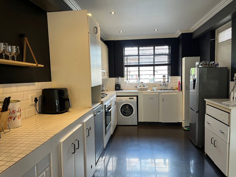 A functional kitchen featuring tiled countertops, built-in cabinetry, integrated laundry plumbing, and a built-in oven, finished with dark wall accents and tiled flooring.