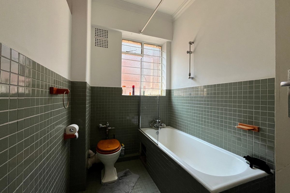 A functional bathroom featuring a bathtub with a shower mixer, glass screen, and classic green tiled walls and flooring.