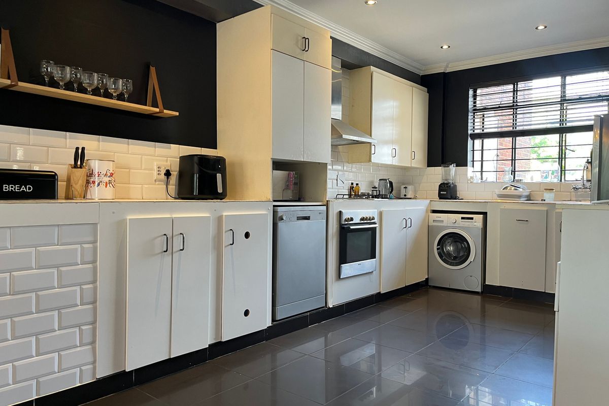A functional kitchen featuring white cabinetry, subway tile backsplash, dark tiled flooring, and integrated appliances including an oven, dishwasher, and washing machine.