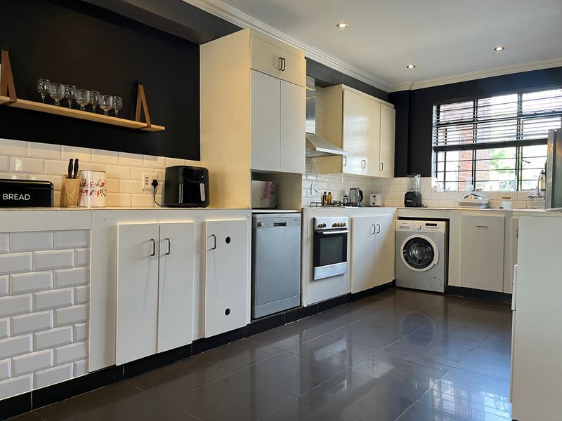 A functional kitchen featuring white cabinetry, subway tile backsplash, dark tiled flooring, and integrated appliances including an oven, dishwasher, and washing machine.