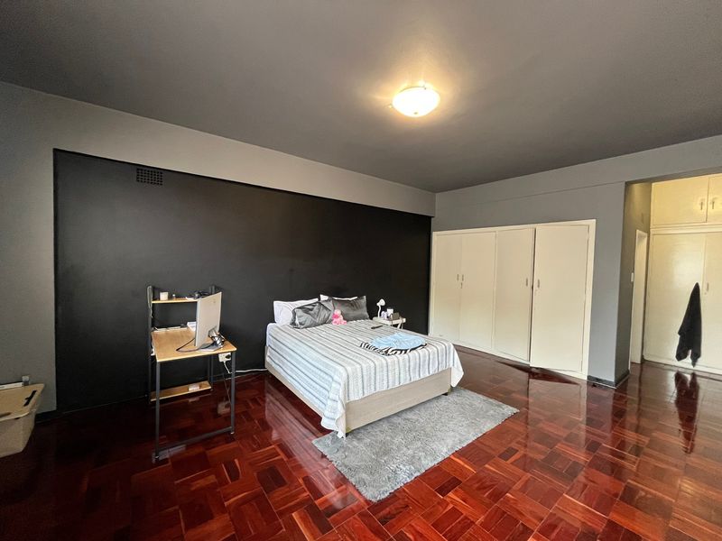 Spacious bedroom featuring polished parquet flooring, a dark accent wall, and extensive built-in cupboard storage.