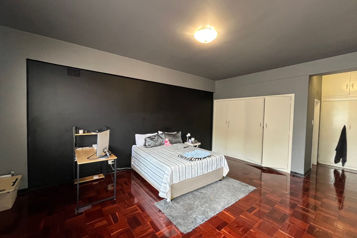 Spacious bedroom featuring polished parquet flooring, a dark accent wall, and extensive built-in cupboard storage.
