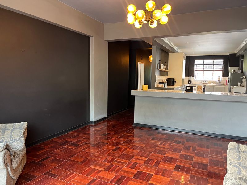 Open-plan living and kitchen area featuring rich parquet flooring, a breakfast bar, and a functional kitchen layout with ample cabinetry.