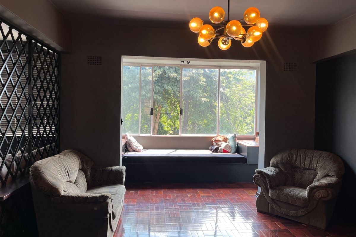 A living room featuring polished parquet flooring, a built-in window seat with garden views, and a decorative metal screen divider.