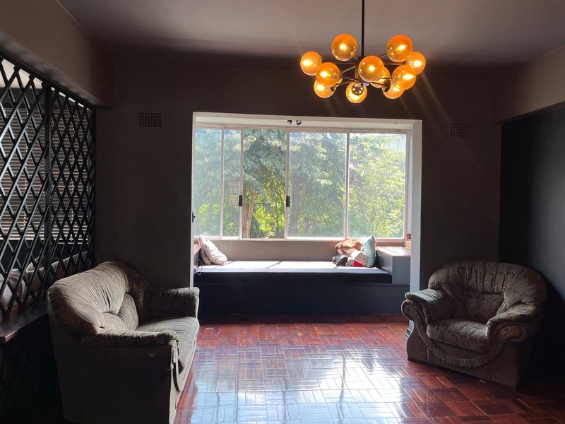 A living room featuring polished parquet flooring, a built-in window seat with garden views, and a decorative metal screen divider.