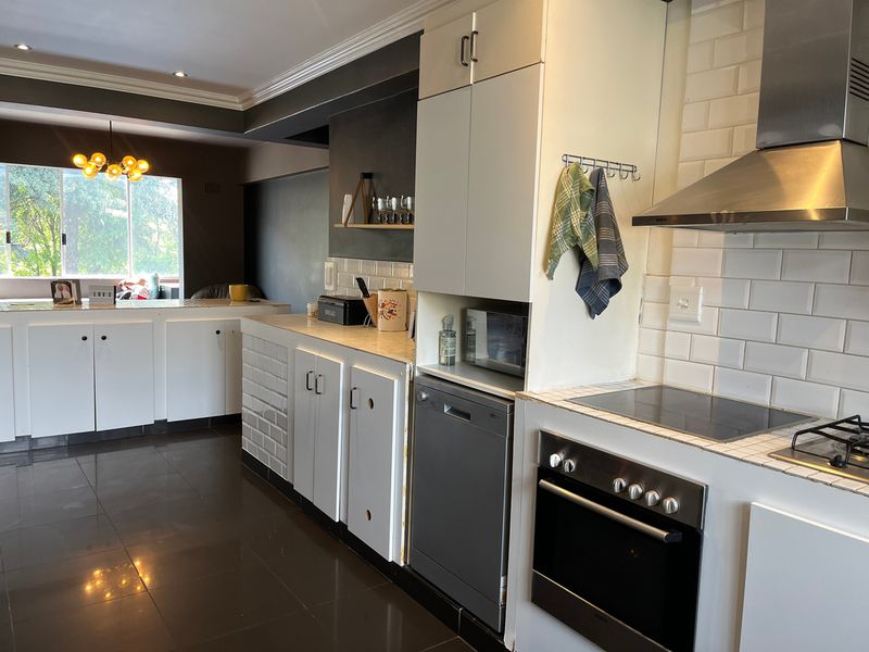 Open-plan kitchen featuring white cabinetry, subway tile backsplash, integrated appliances, and dark tiled flooring, seamlessly flowing into the adjacent living area.