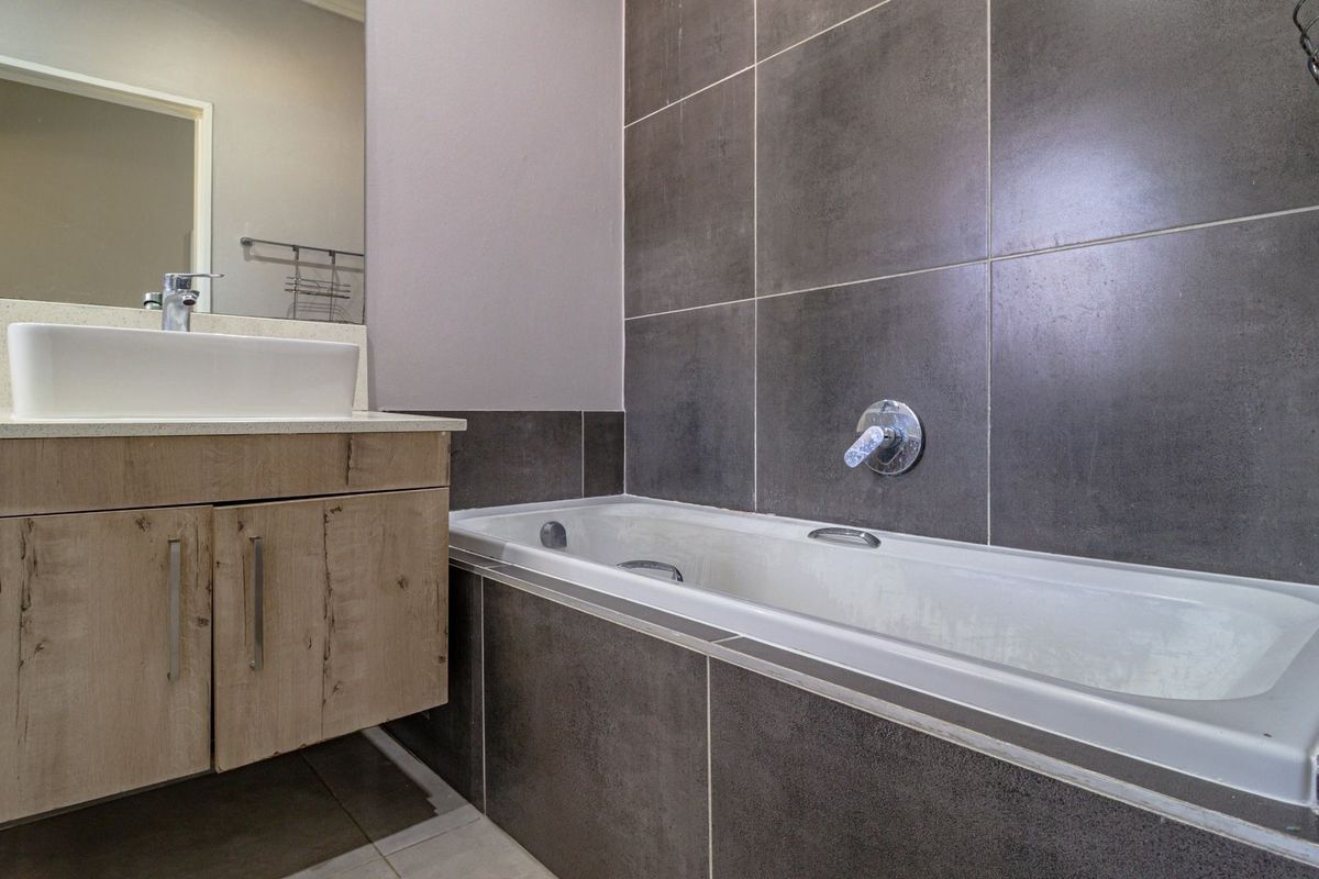 Modern bathroom featuring a built-in vanity with countertop basin, large wall mirror, and a tiled bathtub surround with chrome fixtures.
