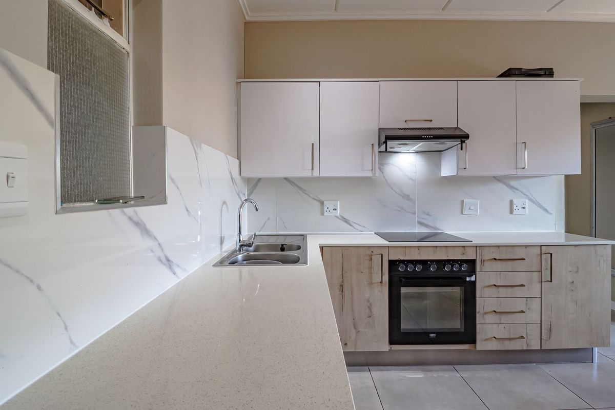 Modern kitchen featuring marble-look splashbacks, quartz countertops, built-in oven, electric hob, extractor fan, and ample upper and lower cabinetry.
