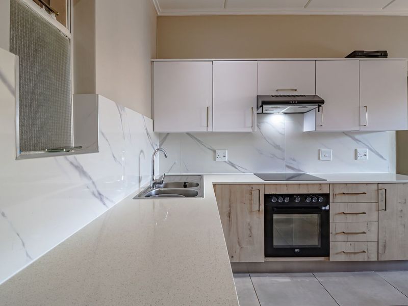 Modern kitchen featuring marble-look splashbacks, quartz countertops, built-in oven, electric hob, extractor fan, and ample upper and lower cabinetry.