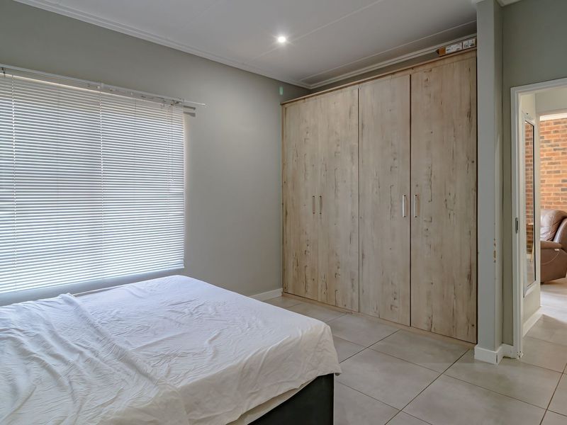 A well-maintained bedroom featuring neutral tiled flooring, modern built-in cupboards with a wood-grain finish, and adjustable venetian blinds.
