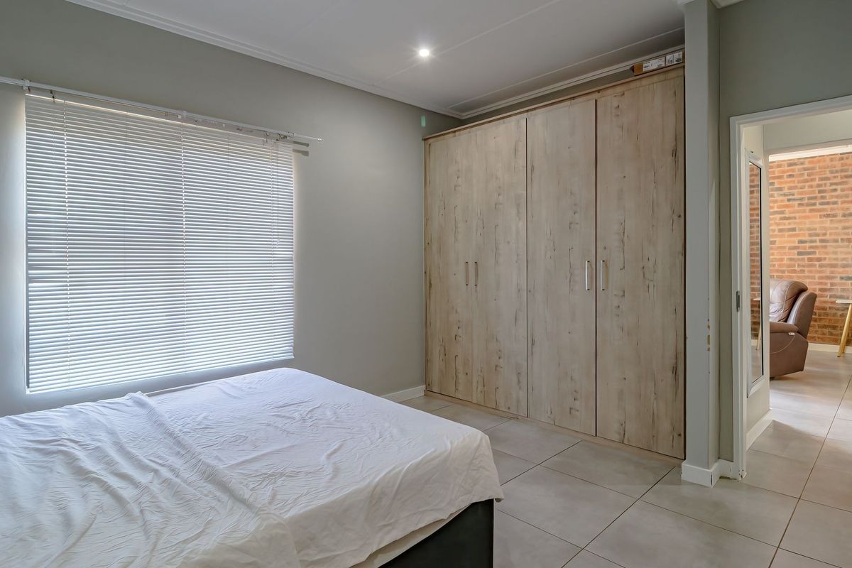 A well-maintained bedroom featuring neutral tiled flooring, modern built-in cupboards with a wood-grain finish, and adjustable venetian blinds.