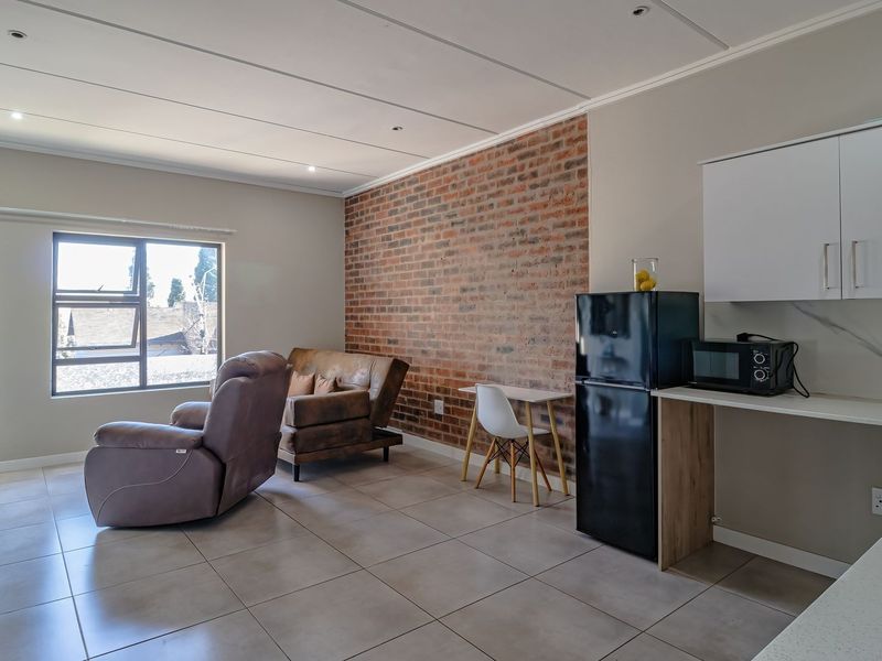 Spacious open-plan living area featuring an exposed brick accent wall, tiled flooring, modern kitchen cabinetry, and direct access to a balcony.
