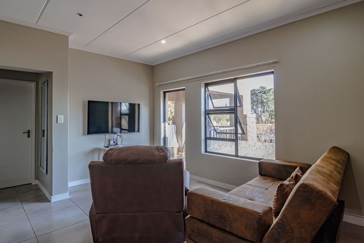 A well-lit living room featuring neutral wall tones, tiled flooring, and large aluminium windows providing natural light and access to an outdoor area.