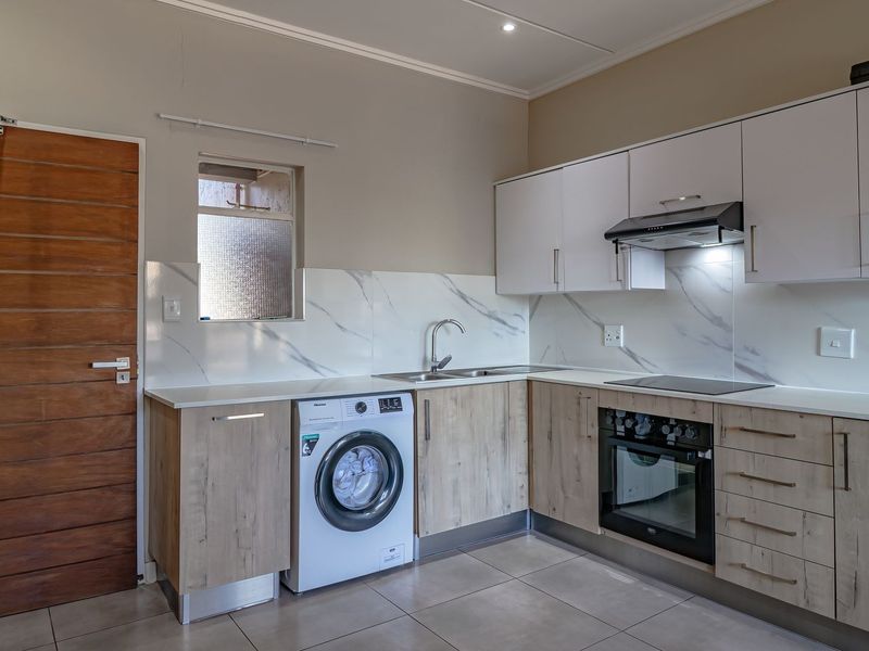 Modern kitchen featuring light wood-finish cabinetry, marble-look splashbacks, integrated oven and hob, and tiled flooring.