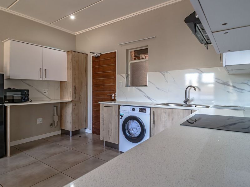 Modern kitchen featuring sleek cabinetry, stone countertops, marble-look splashback, integrated hob, extractor fan, and dedicated space for laundry appliances.
