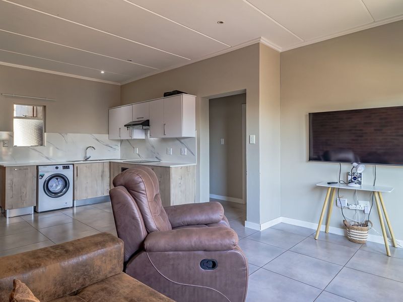 Open-plan living area featuring a modern kitchen with built-in cabinetry, marble-look splashback, and tiled flooring throughout the space.