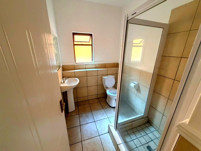 A functional bathroom featuring a pedestal basin, toilet, and a glass-enclosed shower with neutral ceramic tiling throughout.