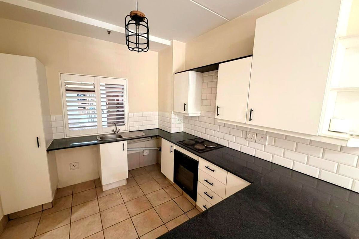 A clean, functional kitchen featuring white cabinetry, dark granite countertops, subway tile backsplash, and built-in oven with electric hob.