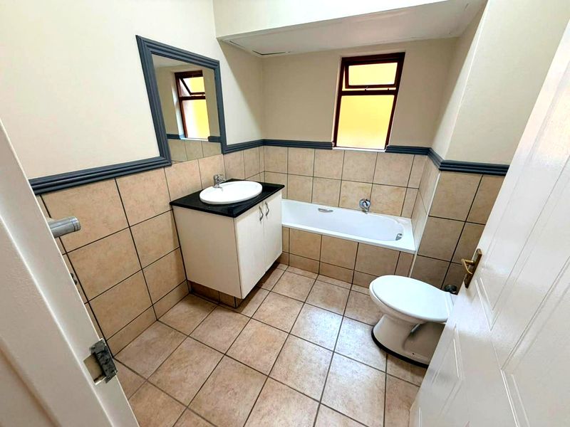 A functional bathroom featuring a vanity with basin, bathtub, toilet, and neutral wall and floor tiling.