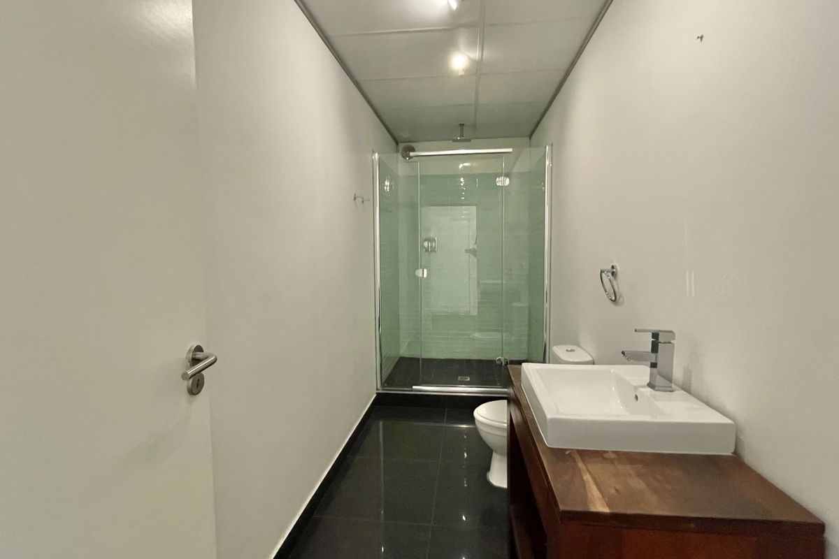 A clean, modern bathroom featuring a glass-enclosed shower, a vanity basin with a wooden cabinet, and dark tiled flooring.