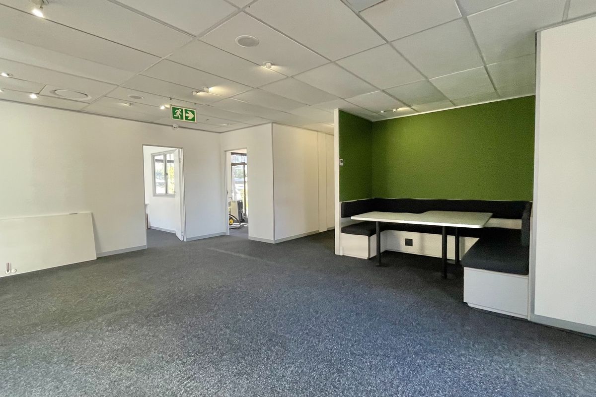 Modern office space featuring a suspended ceiling, recessed lighting, carpeted flooring, and a built-in booth seating area.
