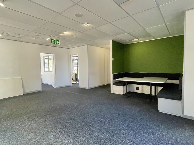 Modern office space featuring a suspended ceiling, recessed lighting, carpeted flooring, and a built-in booth seating area.