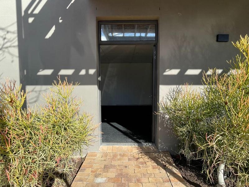 Exterior view of an office entrance featuring a brick paved walkway, metal door frame with transom window, and exterior wall lighting.