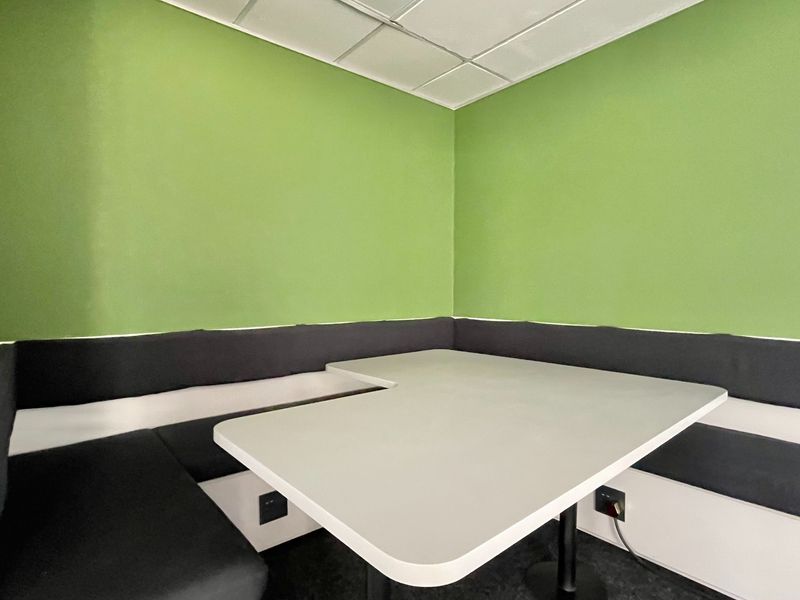 A compact office breakout space featuring built-in corner bench seating, an integrated table, and convenient electrical outlets for workspace connectivity.