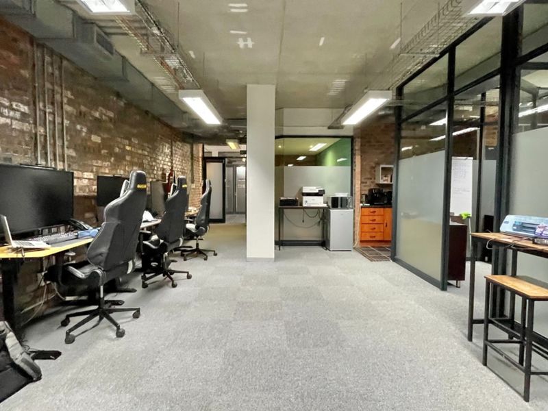 Modern industrial-style office space featuring exposed brick walls, concrete ceilings, glass partitions, and integrated cable management systems.