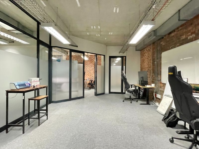 Modern industrial-style office space featuring exposed brick walls, glass partitions, and open-plan layout with functional cable management and professional lighting.